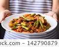Stir fried asparagus with kimchi cabbage and pork on white plate holding by woman hand, Korean style 142790879