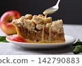 Apple crumble pie slice on a white plate with caramel sauce poured from a spoon 142790883