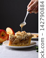 Apple crumble pie slice on a white plate with caramel sauce poured from a spoon 142790884