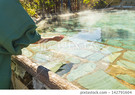 女人的手輕輕地撫摸著露天浴池裡的水。 女人的手輕輕地撫摸著露天浴池裡的水。 142791604