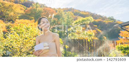 A middle-aged woman enjoying an open-air bath surrounded by autumn foliage. A middle-aged woman enjoying an open-air bath surrounded by autumn foliage. 142791609