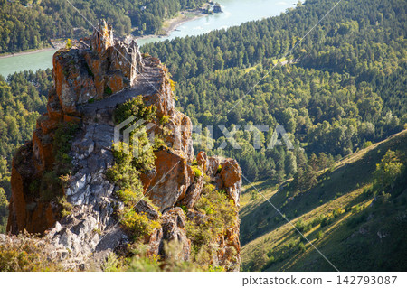 A rugged rocky cliff rises above a winding turquoise river and dense pine forest A rugged rocky cliff rises above a winding turquoise river and dense pine forest 142793087