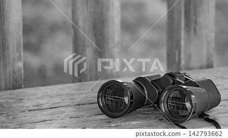 Monochrome still life of binoculars placed on a tree. 142793662