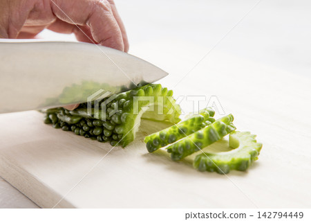 雙手正用刀將已經去籽的苦瓜切成薄片。 142794449