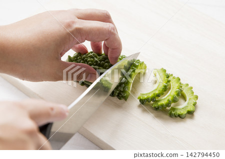 雙手正用刀將已經去籽的苦瓜切成薄片。 142794450
