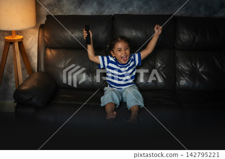 cheerful preschool child girl watching sport tv and celebration with arm raised in the living room at night cheerful preschool child girl watching sport tv and celebration with arm raised in the living room at night 142795221