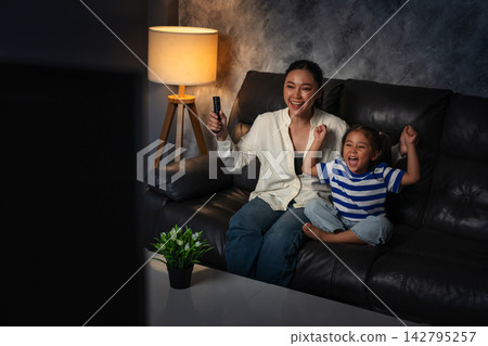 cheerful mother and daughter watching sport tv and celebration with arm raised in the living room at night cheerful mother and daughter watching sport tv and celebration with arm raised in the living room at night 142795257