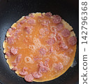 Thai-style omelet with fermented pork sausage (naem) cooking in a hot frying pan. 142796368