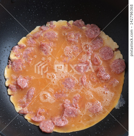 Thai-style omelet with fermented pork sausage (naem) cooking in a hot frying pan. Thai-style omelet with fermented pork sausage (naem) cooking in a hot frying pan. 142796368