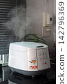 An electric rice cooker boiling with steam rising from it. 142796369