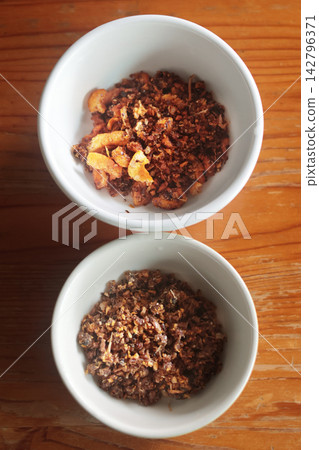 Pork crackling chili dip and ground fish chili dip in small white bowls on a wooden table. Pork crackling chili dip and ground fish chili dip in small white bowls on a wooden table. 142796371