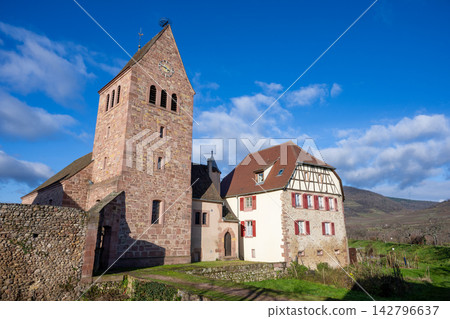 Kienzheim, France: A beautiful landscape where the historic church clock tower and traditional half-timbered buildings stand out against the blue sky. Kienzheim, France: A beautiful landscape where the historic church clock tower and traditional half-timbered buildings stand out against the blue sky. 142796637