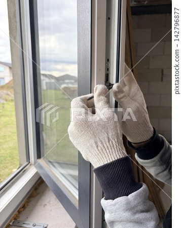 A worker adjusts the mechanism of a modern window frame. Manual window frame adjustment A worker adjusts the mechanism of a modern window frame. Manual window frame adjustment 142796877