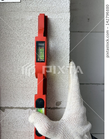 A builder checks the level of an aerated concrete wall using a spirit level. A builder checks the level of an aerated concrete wall using a spirit level. 142796880