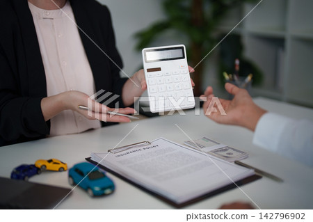 Car insurance agent showing calculator to client for vehicle finance policy Car insurance agent showing calculator to client for vehicle finance policy 142796902