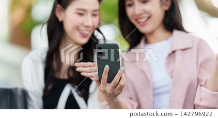 Asian Female Friends Looking at Smartphone Screen Outdoors 142796922