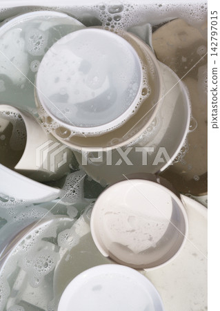 Ceramic plates and bowls soaking in soapy water with bubbles. 142797015
