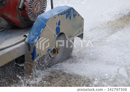 A walk-behind concrete cutter machine, concrete cutter blade spinning with water. A walk-behind concrete cutter machine, concrete cutter blade spinning with water. 142797308