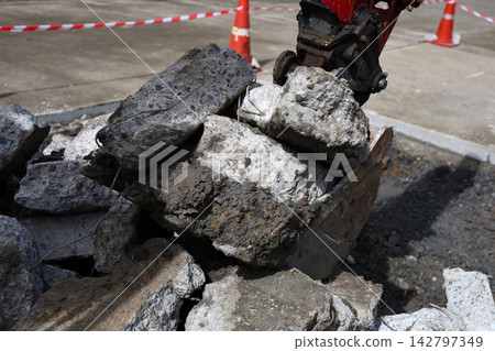 Close-up of an excavator bucket scooping heavy concrete pieces from a pile at a construction site. Close-up of an excavator bucket scooping heavy concrete pieces from a pile at a construction site. 142797349