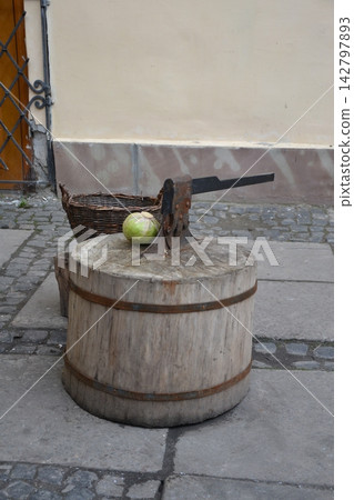 Traditional wooden chopping block with an antique cleaver, fresh cabbage and a wicker basket on a rustic street. Concept of traditional food preparation, rural lifestyle, craftsmanship and vintage 142797893