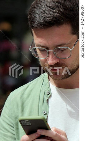 Vertical video. Portrait of casual man using smartphone outdoor. Cheerful man typing messages on phone outside. Online, messaging and browsing internet. Vertical video. Portrait of casual man using smartphone outdoor. Cheerful man typing messages on phone outside. Online, messaging and browsing internet. 142798007