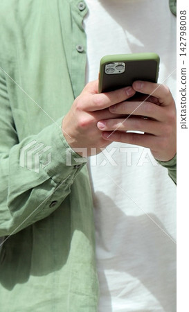 Vertical video. Portrait of casual man using smartphone outdoor. Cheerful man typing messages on phone outside. Online, messaging and browsing internet. Vertical video. Portrait of casual man using smartphone outdoor. Cheerful man typing messages on phone outside. Online, messaging and browsing internet. 142798008