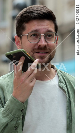 Vertical video. Man recording audio message on smartphone while walking in the city. Using smartphone for voice messages outdoors. Online voice call. Vertical video. Man recording audio message on smartphone while walking in the city. Using smartphone for voice messages outdoors. Online voice call. 142798011