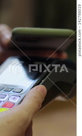 Vertical video. Closeup man hand paying with mobile phone over pos terminal with NFC technology. Man using smartphone for wireless money transfer. Vertical video. Closeup man hand paying with mobile phone over pos terminal with NFC technology. Man using smartphone for wireless money transfer. 142798019