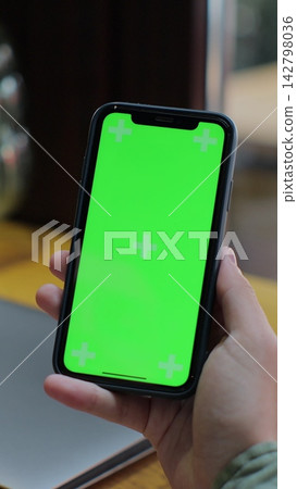 Vertical video. Over the shoulder view of man using green screen smartphone in the cafe. Mock-up for tracking. Watching content video blog and surfing internet. Vertical video. Over the shoulder view of man using green screen smartphone in the cafe. Mock-up for tracking. Watching content video blog and surfing internet. 142798036