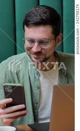 Vertical video. Young person working on laptop and checking smartphone in a cafe. Vertical video. Young person working on laptop and checking smartphone in a cafe. 142798174