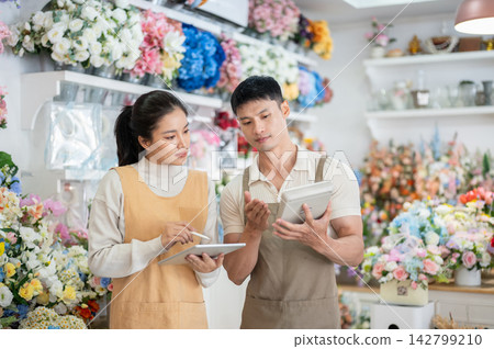 Asian man woman florist reviewing business cost on calculator surrounded by colorful flowers in shop Asian man woman florist reviewing business cost on calculator surrounded by colorful flowers in shop 142799210