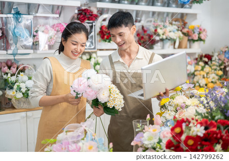 Asian man and woman florist couple discussing flower arrangements while using a laptop in their shop Asian man and woman florist couple discussing flower arrangements while using a laptop in their shop 142799262