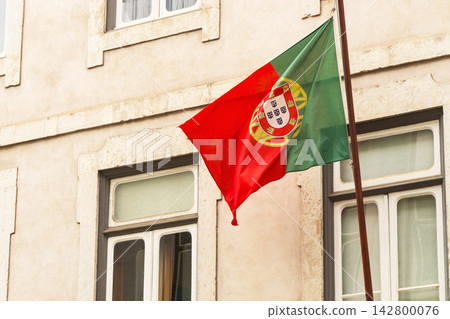 Portugal flag waves in Lisbon against a building with open windows Portugal flag waves in Lisbon against a building with open windows 142800076