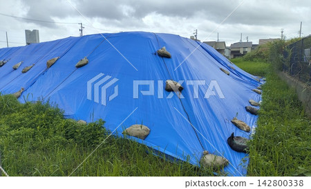 Construction site where soil and materials are covered with blue tarpaulins and secured with sandbags. Construction site where soil and materials are covered with blue tarpaulins and secured with sandbags. 142800338