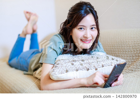 A woman lying on the sofa and using a smartphone A woman lying on the sofa and using a smartphone 142800970