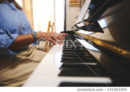 Woman playing piano at home, close-up of hands on keyboard with sheet music Woman playing piano at home, close-up of hands on keyboard with sheet music 142801003