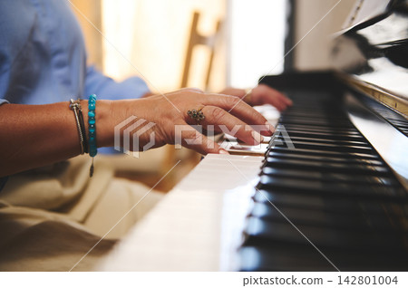 Woman playing piano with close-up of hands, rings and bracelets on acoustic keyboard Woman playing piano with close-up of hands, rings and bracelets on acoustic keyboard 142801004