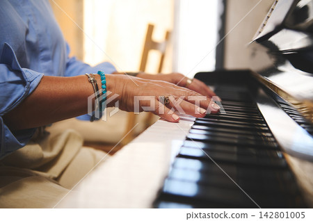 Woman playing piano at home - close-up of hands on keyboard with bracelet 142801005