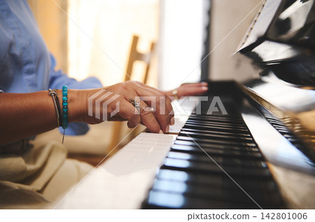 Woman playing piano with turquoise bracelet, close-up on hands practicing on a grand piano at home Woman playing piano with turquoise bracelet, close-up on hands practicing on a grand piano at home 142801006