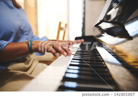Woman playing piano, hands close-up in warm sunlit home interior Woman playing piano, hands close-up in warm sunlit home interior 142801007