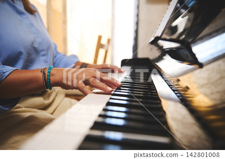 Woman playing piano at home - close-up of hands on keys with warm sunlight Woman playing piano at home - close-up of hands on keys with warm sunlight 142801008