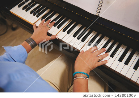 Woman playing piano with sheet music, hands on keys practicing a melody in close-up Woman playing piano with sheet music, hands on keys practicing a melody in close-up 142801009