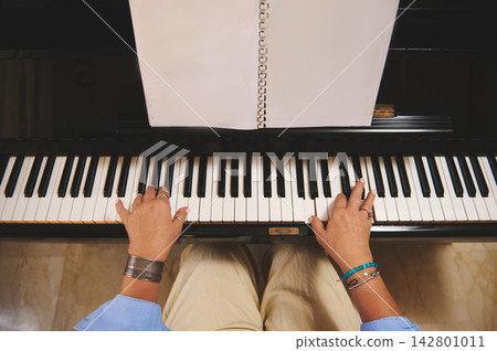 Woman playing piano with sheet music on upright piano, hands on keys practicing classical piece Woman playing piano with sheet music on upright piano, hands on keys practicing classical piece 142801011