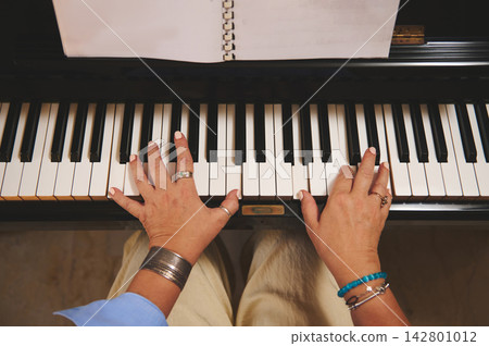 Woman playing piano with sheet-music, hands on keys practicing melody Woman playing piano with sheet-music, hands on keys practicing melody 142801012