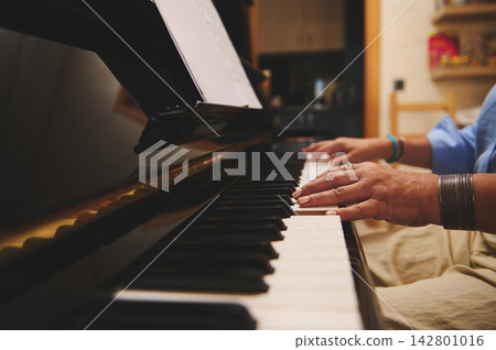 Woman playing piano at home with sheet music and focused hands Woman playing piano at home with sheet music and focused hands 142801016