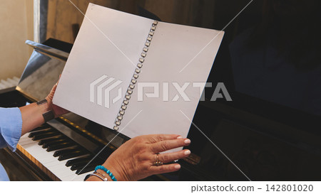 Woman practicing piano at home reading sheet music on an upright piano Woman practicing piano at home reading sheet music on an upright piano 142801020