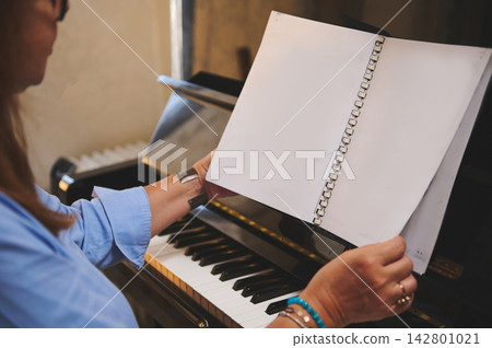 Woman turning sheet music pages on piano during a focused practice session Woman turning sheet music pages on piano during a focused practice session 142801021