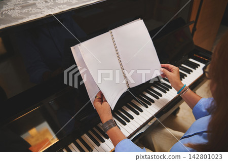 Woman turning sheet music at a piano keyboard preparing to practice a classical piece Woman turning sheet music at a piano keyboard preparing to practice a classical piece 142801023