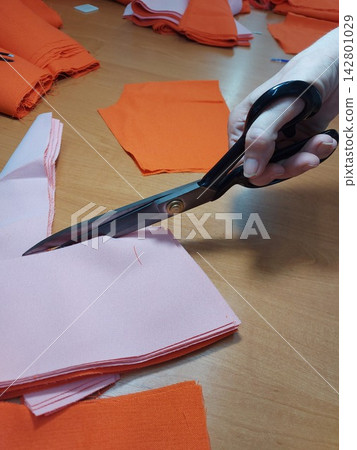 scissors cutting fabric on table with focused and precise top-down view in crafting setting with black and orange materials and clean background, editorial and educational content. scissors cutting fabric on table with focused and precise top-down view in crafting setting with black and orange materials and clean background, editorial and educational content. 142801029