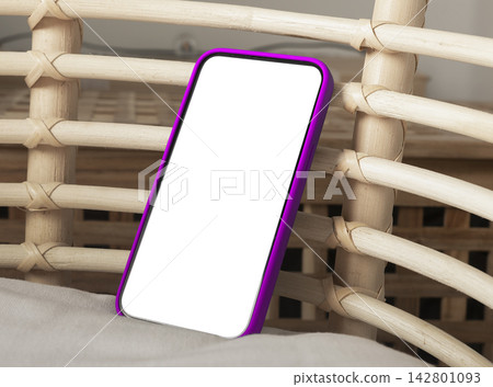 Blank smartphone mockup with purple case on wicker furniture. Angled mobile phone with white screen in a cozy indoor setting. App design and advertising template with copy space.. Blank smartphone mockup with purple case on wicker furniture. Angled mobile phone with white screen in a cozy indoor setting. App design and advertising template with copy space.. 142801093